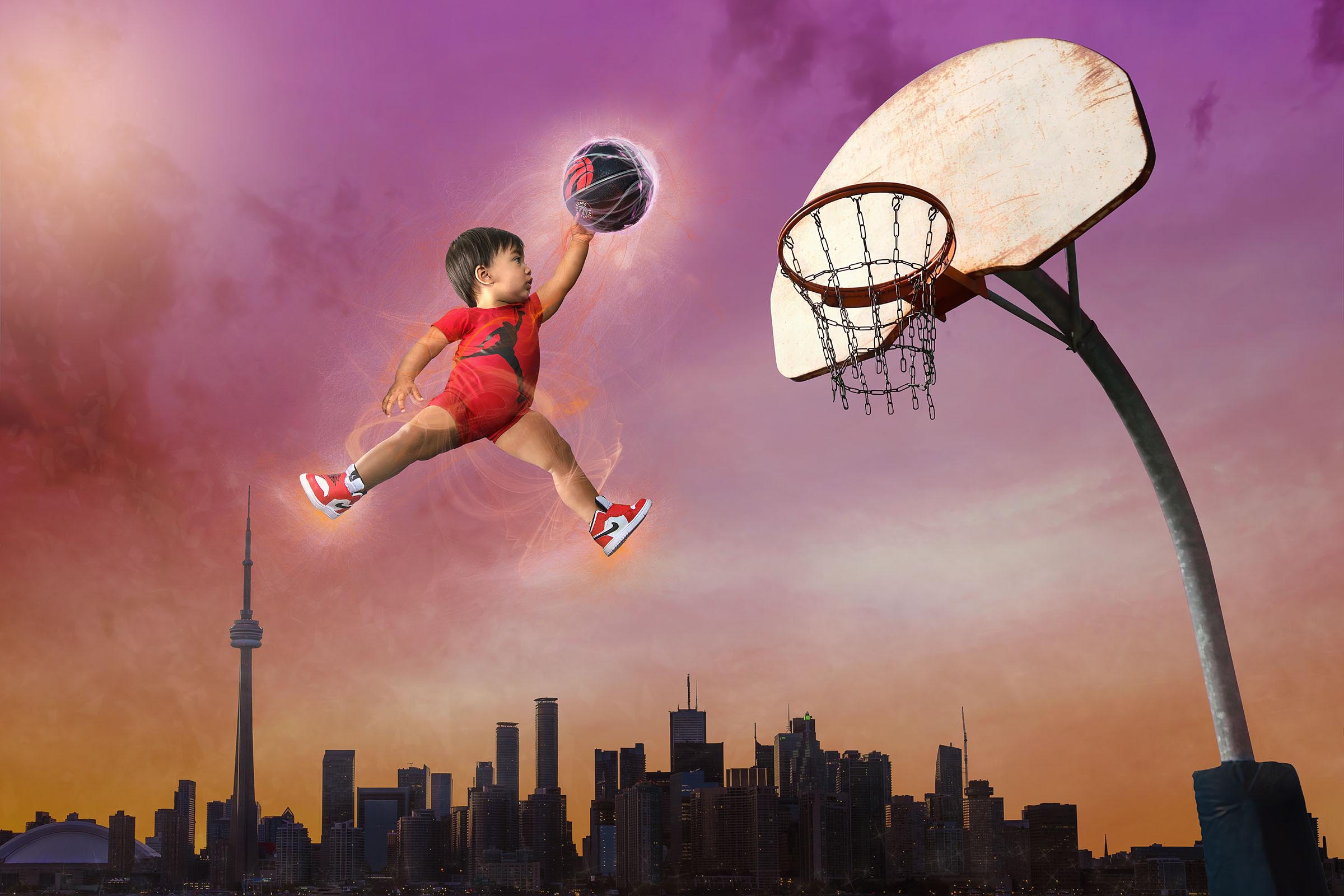 Composite of baby boy flying in the air dunking a Toronto Raptors basketball into a hoop with city of Toronto background by Vaudreuil-Soulanges and West Island of Montreal photographer Tobi Malette