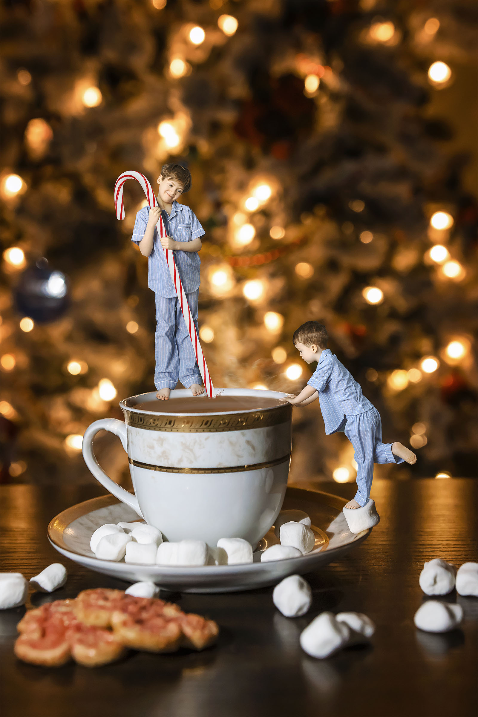 Composite of two boys wearing blue pyjamas one boy standing on a mug stirring with candycane other boy standing side on marshmallow christmas tree background by Vaudreuil-Soulanges and West Island of Montreal photographer Tobi Malette